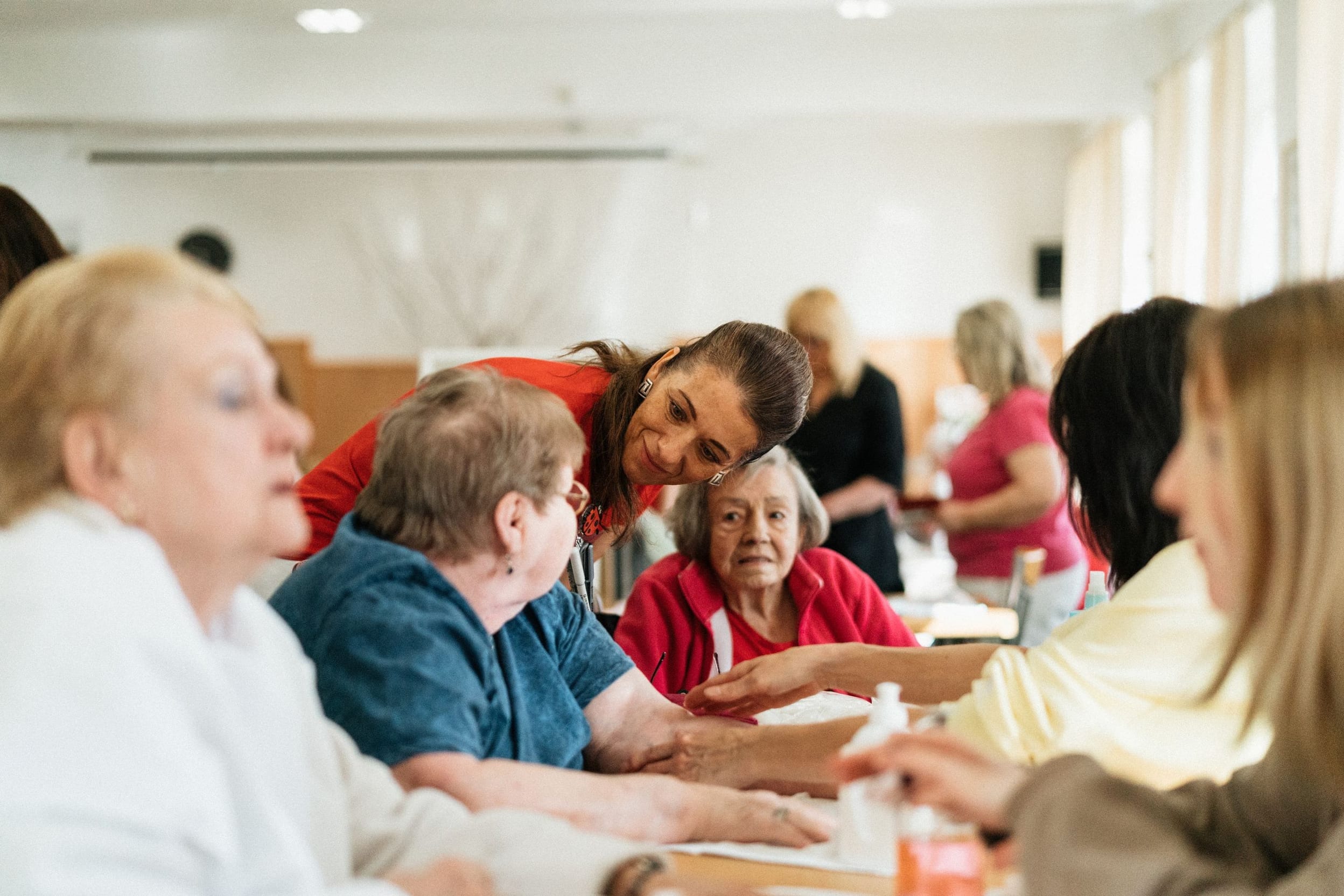 Residents and a care worker chatting warmly in the sunlit common room of an assisted-living home.