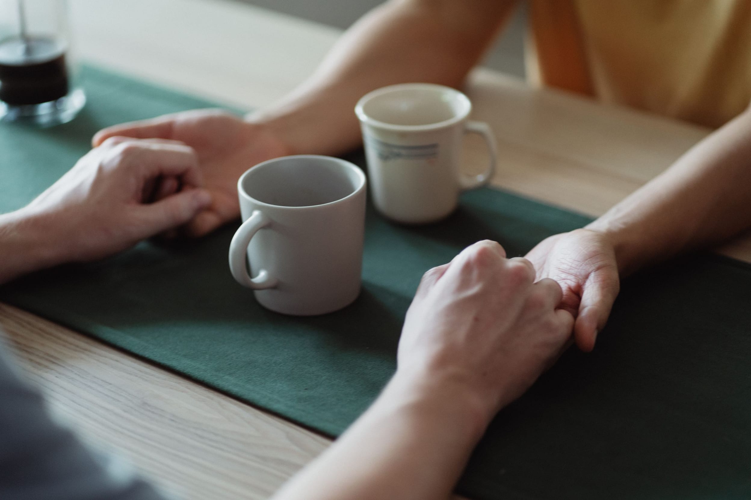 Two people holding hands across a kitchen table in a calm, sunlit home.