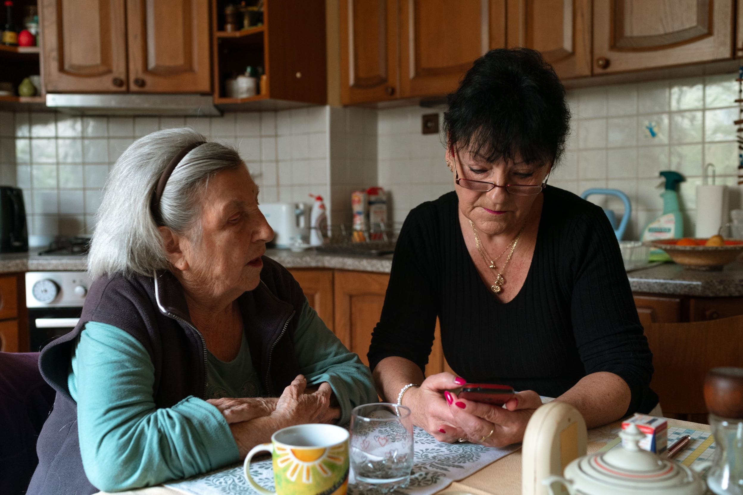 A caregiver helping an older client with a daily task in a bright home kitchen.